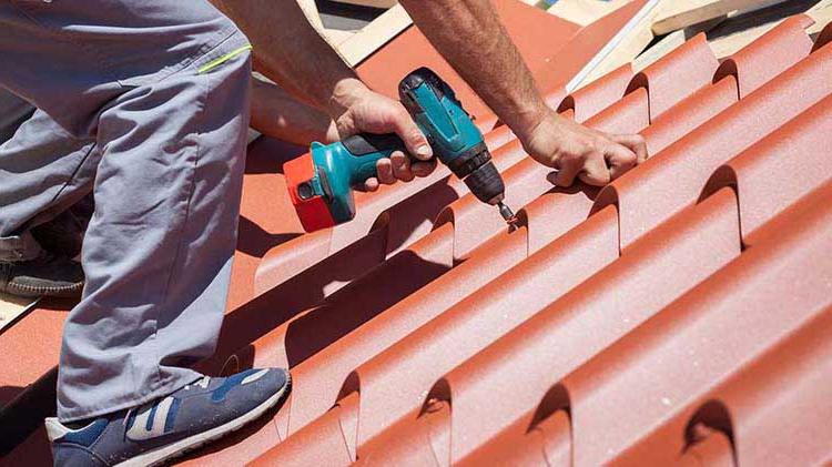 A contractor screws down another roofing tile.